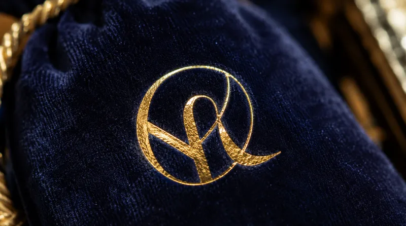 Hot stamping fabric macro view showing gold foil logo on deep velvet pouch with shimmering metallic finish