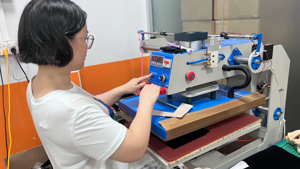 Fabric Pouch Heat Press Operation Operator using an industrial heat press machine on a light-colored fabric piece in a workshop