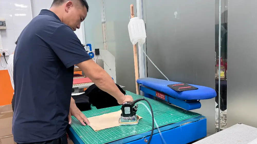 Fabric Pouch Pressing Workstation Worker pressing a light-colored fabric piece on a cutting mat beside a blue heat press machine in a workshop