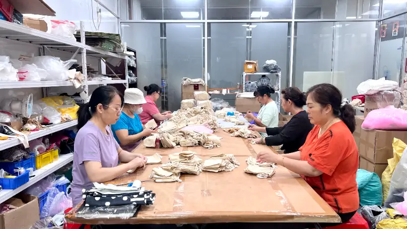 Fabric Pouch Worktable Workers handling assorted fabric pouches at a shared worktable in a packaging workshop