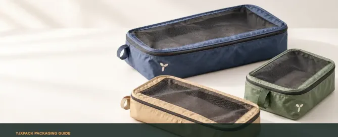 Three custom packing cubes in navy, forest green and sand with mesh top panels and abstract logo marks