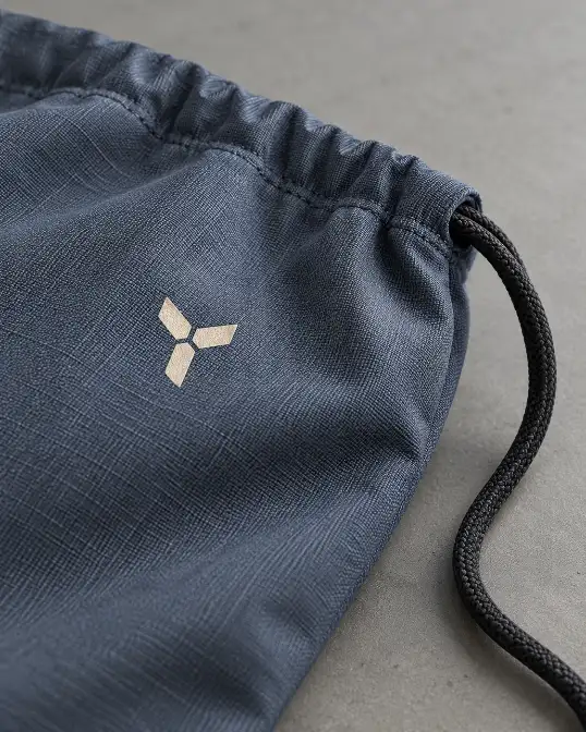 Toiletry Bag Logo and Drawstring Detail Close view of a navy fabric toiletry bag with an abstract logo mark, drawstring cord and textured material