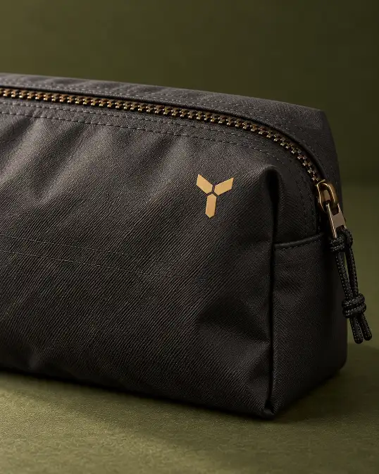 Toiletry Bag Logo and Zipper Finish Close view of a black toiletry bag with abstract logo mark, zipper teeth and stitched fabric surface